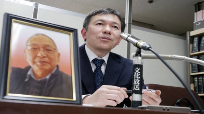 Putra Shizuo Aishima di samping foto ayahnya, yang meninggal usai ditahan 