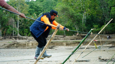 Bupati Aceh Tengah Haili Yoga berjalan di jembatan darurat terbuat dari tali.
