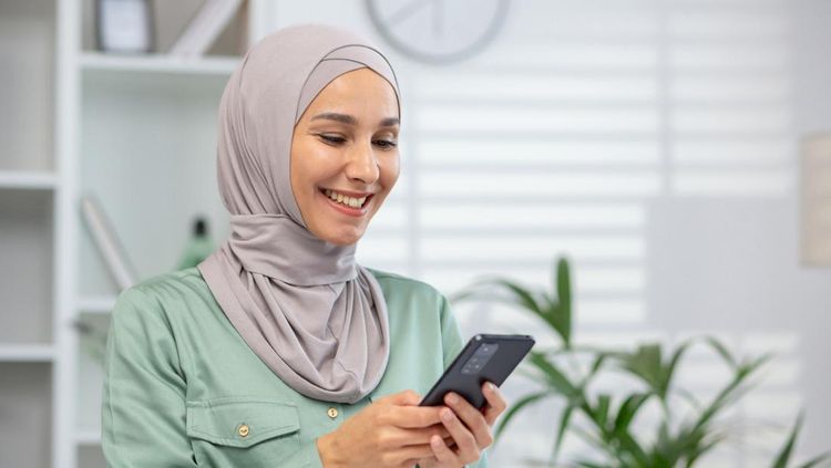 Cheerful Muslim woman wearing a hijab engages with her smartphone&amp;comma; portraying connectivity and modern lifestyle&amp;period;, Syarat pembuatan SKCK online untuk melamar kerja, Biaya pembuatan SKCK online, Cara membuat SKCK online untuk melamar kerja, Ketentuan dalam membuat Surat Keterangan Catatan Kepolisian (SKCK)