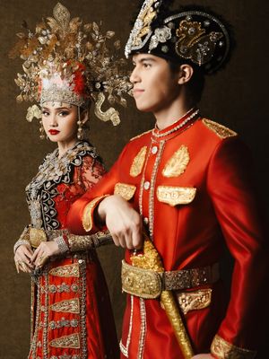 7 Detail Busana Adat Gorontalo Syifa Hadju dan El Rumi saat Prewedding, Serba Merah, 1. Dominasi warna merah yang menjadi pusat perhatian, 2. Mahkota tinggi dengan ornamen emas pada busana Syifa, 3. Detail payet penuh di bagian dada dan bahu, 4. Lengan transparan dengan payet merah, 5. Sabuk emas lebar sebagai penegas siluet, 6. Busana El Rumi bergaya formal dengan aksen emas, 7. Perpaduan keseluruhan tampak serasi dan berkarakter