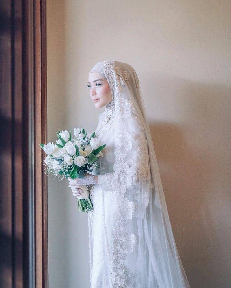 instagram.com/hamidahrachmayanti, 1. Tampil manis dengan kebaya khas Sunda yang sederhana. Lengkap dengan siger atau mahkota pernikahan khas adat Sunda., 2. Dress putih model brokat yang simpel bisa jadi pilihan untuk kamu yang anti ribet. Supaya lebih spesial, tambahkan aksesori di atas kepala dengan veil yang anggun., 3. Jangan ragu coba pakai kebaya model off-shoulder di hari pernikahan. Detail pearl pada kebaya dijamin membuat penampilan jadi lebih maksimal., 4. Bergaya a la putri keraton Yogyakarta dengan kebaya adat Jawa yang anggun. Andalkan kebaya klasik model kutubaru dengan aksen bordir yang menutupi bagian pundak., 5. Lace dress dengan dasar warna putih memang tidak pernah gagal untuk baju akad nikah yang elegan. Makin sempurna dengan hiasan kepala berupa tudung pernikahan yang seragam dengan bahan gaun.