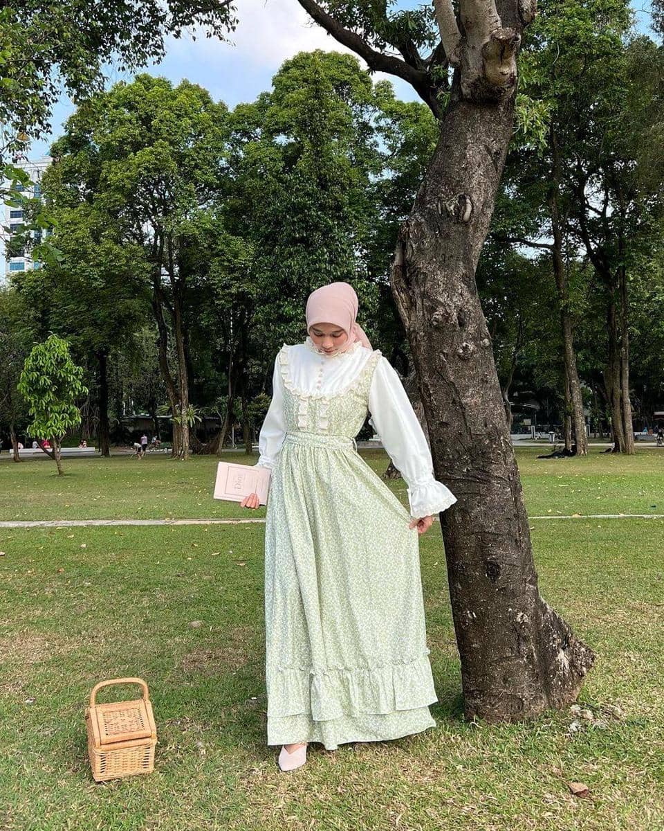 instagram.com/nasariastri, 1. Tampil layaknya cewek pedesaan dengan vintage dress bernuansa hijau pastel. Padu-padankan dengan white heels dan hijab pink untuk mempermanis penampilan., 2. Gaya cottagecore yang effortless, coba kenakan silk dress warna putih polos yang simpel. Cocok dipasangkan dengan polkadot hijab dan sandal heels berwarna senada., 3. Ciptakan gaya feminin a la pedesaan Eropa dengan puff-sleeves dress motif kotak-kotak. Andalkan nuansa warna pink supaya lebih maksimal., 4. Padu-padan cottagecore yang satu ini cocok dipakai buat pergi piknik! Kenakan maxi dress warna biru, lengkap dengan aksesori neck scarf dan straw hat yang modis., 5. Bersantai di depan rumah, makin manis dengan gaya cottage core. Kombinasi white blouse dan plaid skirt bisa jadi andalan. Nggak ketinggalan aksesori flower crown sebagai penunjang penampilan.