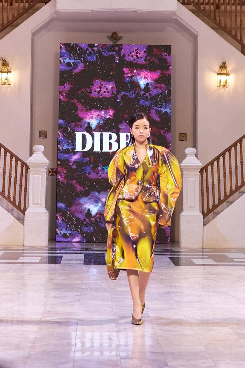 DIBBA - Fall Winter 2025 - Runway - Thailand Fashion Week - 18.jpg, 1. Berinovasi pada material, Odyssey memperkenalkan tekstil inovatif seperti printed crystal mesh & kain aktif termal yang diyakini akan hits di 2026, 2. Material dinamis ini tidak hanya menantang desain konvensional, tetapi menegaskan pendekatan avant-garde DIBBA terhadap fungsionalitas & tekstur, 3. Setiap karya dalam koleksi ini berperan sebagai bab dalam narasi kosmik, yang mengubah model menjadi pengelana dalam lanskap mimpi futuristik, 4. Odyssey dari DIBBA membayangkan kembali fashion sebagai wahana penemuan, tempat gaya bertemu hal-hal yang belum dikenal melalui imajinasi, 5. Presentasi ini menegaskan pengaruh global DIBBA dengan narasi lintas budaya dan semangat eksperimental untuk audiens dunia