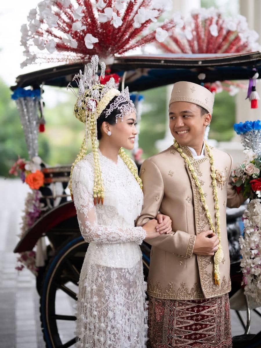 get (3).jpg, 1. Namira Adjani menggunakan kebaya putih dengan detail di bagian pinggul terinspirasi dari Kembang Kelapa yang menjadi ciri khas budaya Betawi., 2. Kembang Kelapa memiliki nilai filosofi sebagai lambang kemakmuran dan simbol kehidupan manusia yang bermanfaat, 3. Didiet Maulana juga memberikan aksen rumbai pada bagian dada yang membuat kebaya terlihat semakin menarik., 4. Namira Adjani menggunakan kain batik yang senasa dengan sang suami., 5. Sebagai sentuhan terakhir, Namira Adjani menggunakan headpiece lengkap dengan tusuk konde dan ronce melati