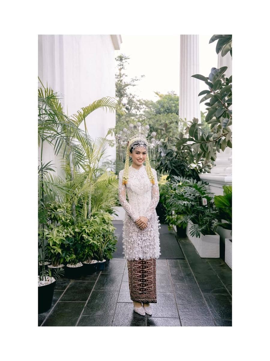 get (2).jpg, 1. Namira Adjani menggunakan kebaya putih dengan detail di bagian pinggul terinspirasi dari Kembang Kelapa yang menjadi ciri khas budaya Betawi., 2. Kembang Kelapa memiliki nilai filosofi sebagai lambang kemakmuran dan simbol kehidupan manusia yang bermanfaat, 3. Didiet Maulana juga memberikan aksen rumbai pada bagian dada yang membuat kebaya terlihat semakin menarik., 4. Namira Adjani menggunakan kain batik yang senasa dengan sang suami., 5. Sebagai sentuhan terakhir, Namira Adjani menggunakan headpiece lengkap dengan tusuk konde dan ronce melati