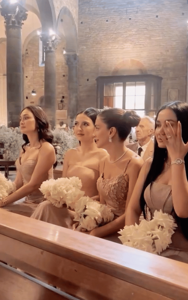 luna-maya-dan-raline-shah-jadi-bridesmaid-millane-fernandez-1754829870985.png, 1. Raline Shah dan Luna Maya diundang menjadi bridesmaids di acara nikahan sang sahabat, Millane Fernandez, yang digelar di Florence, Italia. , 2. Banyak yang salfok dengan penampilan Raline saat hadir di acara pemberkatan pernikahan. Penampilannya elegan dengan gaun dusty pink yang serasi., 3. Gaun yang dipilih Raline Shah memiliki model strapless dengan bagian bawah rok berdetail lipit dengan material lace sebagai lapisan luarnya., 4. Rambut lurusnya ditata simple, digerai dengan tatanan sleek di bagian depan yang membuat keseluruhan penampilannya tetap minimalis namun elegan., 5. Bersama bridesmaid lain, ia juga terlihat mengenakan robe warna gold berbahan lace motif floral yang dipadukan dengan slip dress yang senada.