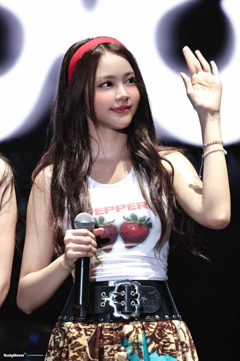 GzHy2t_bkAA1UpM.jpeg, 1. Member asal Indonesia, Carmen unjuk pesona di atas panggung pakai tank top putih, rok mini serta aksesori seperti belt dan bando merah., 2. Ye-On memilih kaos hijau dipadukan rok ruffle unik sementara Stella andalkan crop top motif kotak-kotak dan rok denim dengan detail lipit., 3. Yuha pakai babytee biru dengan rok mini hitam aksen pleats, sementara Ian tampil dengan layering crop top dan rok denim detail grafis., 4. Jiwoo tampil energik di atas panggung pakai tanktop gambar kucing dipadukan rok mini hitam yang punya aksen belt besar., 5. Juun pakai outfit warna coklat dengan tanktop dan rok yang senada. Sementara A-na memilih graphic tee dan rok pleats motif kotak-kotak. 