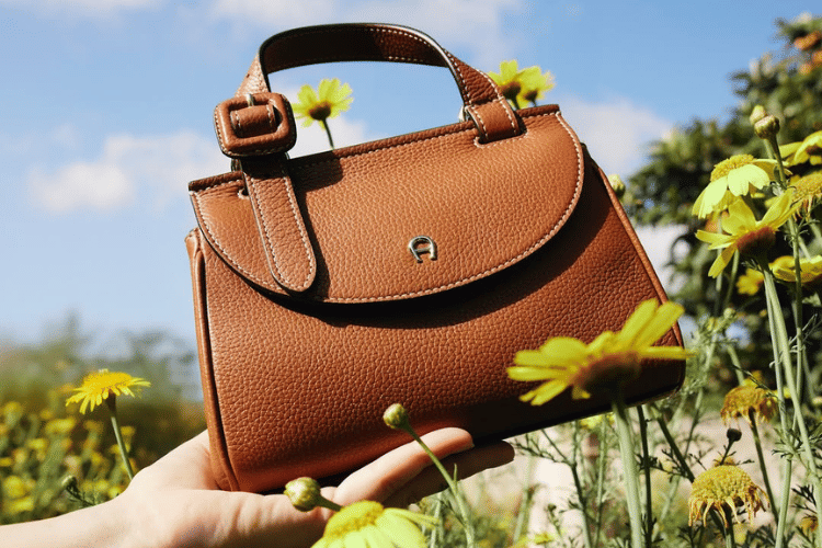 Cover Tas Aigner - instagram.comaignermunich.png, 1. Terbuat dari material yang berkualitas tinggi, 2. Jahitan rapi dan presisi, 3. Logo pada bagian luar tas, 4. Material hardware yang kokoh, 5. Dilengkapi care card dan dust bag eksklusif