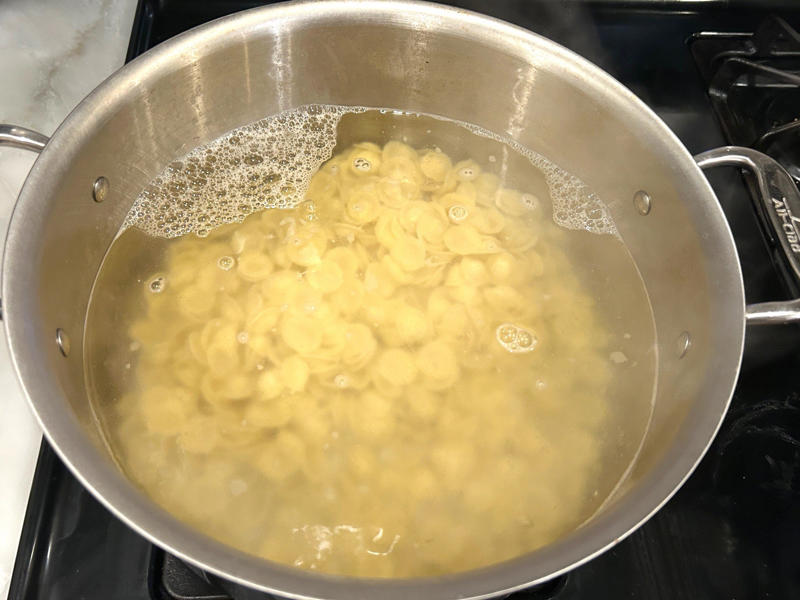 I filled a large pot with water and placed it over the stove, bringing it to a boil before adding the pasta. Ina Garten's orecchiette pasta features two types of sausage and broccoli rabe., First, I preheated the oven to 350 degrees Fahrenheit and prepped the sausages., After cooking the sausages for five minutes, I added the garlic., Then, it was time to add the tomatoes and wine.