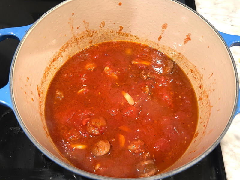 I turned the heat to low so the sauce could simmer while I prepped my pasta. Ina Garten's orecchiette pasta features two types of sausage and broccoli rabe., First, I preheated the oven to 350 degrees Fahrenheit and prepped the sausages., After cooking the sausages for five minutes, I added the garlic., Then, it was time to add the tomatoes and wine.