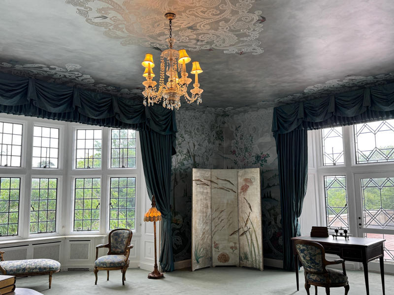There are personalized touches all over the house's limestone exterior., It took three years to complete Coe Hall., One of the first rooms you can view is Coe's den., It's covered in dark wood, giving a masculine atmosphere., The art in the living room is original to the home., It's certainly not a bad place to spend your weekends., The craftsmanship throughout the house was impossible to miss., There was another portrait of Coe hanging in the corner., The main staircase felt straight out of a castle., And no, that's not wallpaper. This design was hand-painted onto the wall., The windows gave her a view of the gardens she painstakingly designed., This is her bathroom. Once again, it's very French., Now it was time to check out the much-revered grounds., Right off the bat, this fountain caught my eye., Can't you just hear someone saying, "Once upon a time…"?, Rogers entertained her friends in the Tea House on nice days., It looks like the inside of a Tiffany's box., Walking through it felt like walking through a storybook., One corner of the building was anchored by this giant palm tree., It has the largest collection of camellias under glass in the northeast., However, camellia season is in January, so we missed it.
