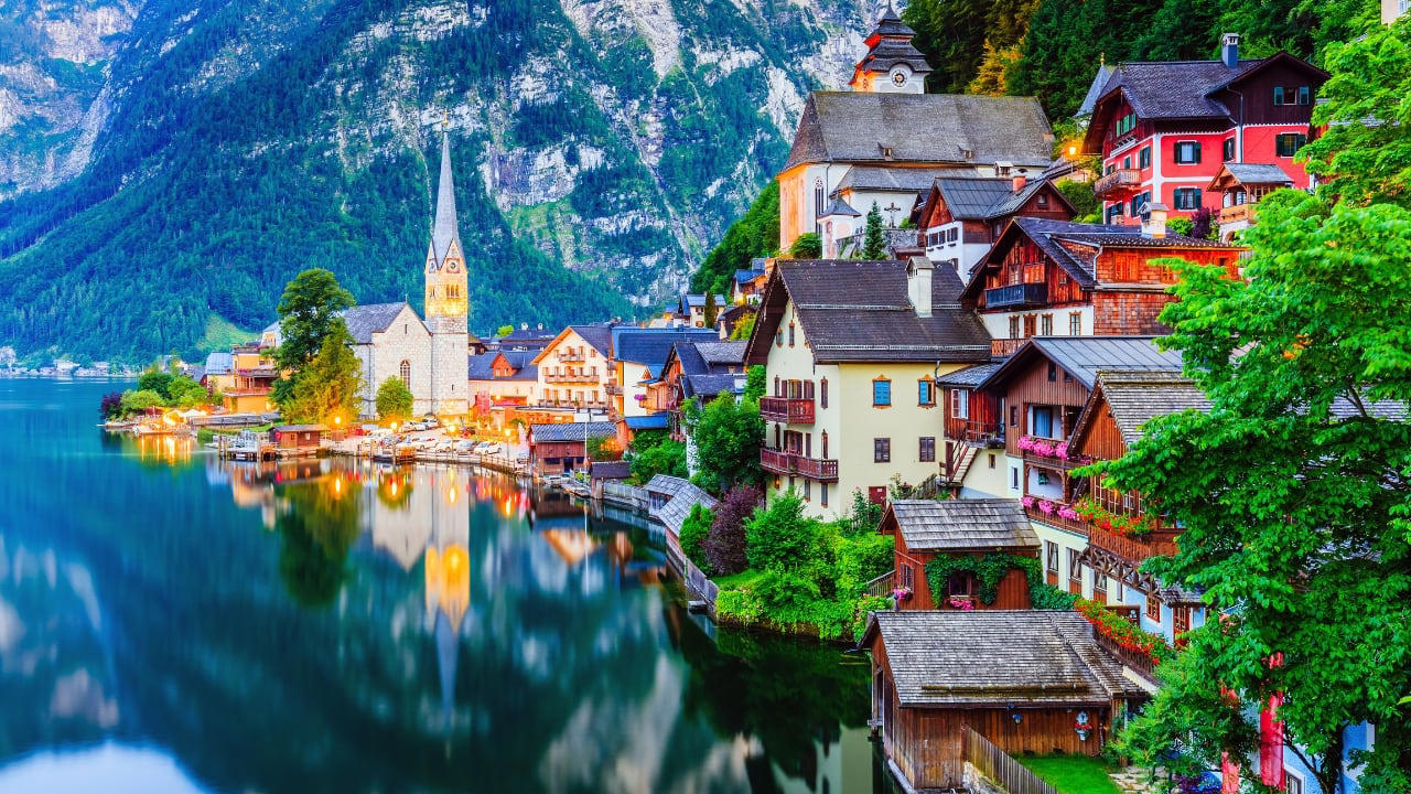 1. Hallstatt, Austria Balanced between lake and limestone, Hallstatt reads like a forgotten chapter from an alpine fable. Its salt-stained history, mirrored waters, and slate-roofed homes draw quiet reverence, not crowds. In winter, it feels paused; in summer, painted. (Image: Canva) 1. Hallstatt, Austria Balanced between lake and limestone, Hallstatt reads like a forgotten chapter from an alpine fable. Its salt-stained history, mirrored waters, and slate-roofed homes draw quiet reverence, not crowds. In winter, it feels paused; in summer, painted. (Image: Canva), 2. Shirakawa-go, Japan Cradled by mountains and wrapped in thatch, Shirakawa-go holds firm to tradition. Its steep-roofed farmhouses, designed to endure snow and time, glow amber at dusk. The seasons arrive like guests—welcomed, noticed, remembered. (Image: Canva), 3. Colmar, France Colmar does not ask for attention—it commands it. With its riot of half-timbered homes, canal reflections, and Alsatian flourishes, it walks the line between theatre and truth. Even its shadows are deliberate. (Image: Canva), 4. Bibury, England Set beside the Coln and stitched into the hills, Bibury whispers of England before speed. Honey-coloured cottages in tight rows, trout streams that glisten without reason, and hedgerows that seem older than maps. (Image: Canva), 5. Giethoorn, Netherlands There are no cars in Giethoorn. Only boats, bridges, and hushed conversations. It is a village that floats, slowly, in its own rhythm. The canals speak softly; the thatched roofs never hurry. (Image: Canva), 6. Reine, Norway Beyond the Arctic Circle lies Reine—a scattering of crimson cabins that appear borrowed from a painting. Mountains rise like frozen waves behind them, and the sea never stops watching. Reine is remote, but never empty. (Image: Canva), 7. Eze, France High above the Riviera, where the cliffs fall into blue, sits Eze—a village of stone and shadow. Its alleys twist upward as if climbing toward memory. Time lingers here, in the scent of thyme and sea. (Image: Canva), 8. Goreme, Turkey Caves carved by wind and wonder—Goreme belongs to the Earth, not to man. Fairy chimneys pierce the sky, and hot-air balloons rise like thoughts at dawn. It is a village of both ground and sky. (Image: Canva), 9. Dinant, Belgium Hemmed in by cliff and river, Dinant feels composed rather than built. Saxophones hang from bridges, limestone watches from above, and the Meuse flows through it like a quiet refrain. Gothic never looked so lyrical. (Image: Canva), 10. Leavenworth, Washington, USA This village is not a replica—it’s a reinvention. Bavarian beams beneath American skies, brats beside apple pie. Surrounded by pine, performance, and peaks, Leavenworth is both celebration and curiosity, wrapped in wood and wonder. (Image: Canva)