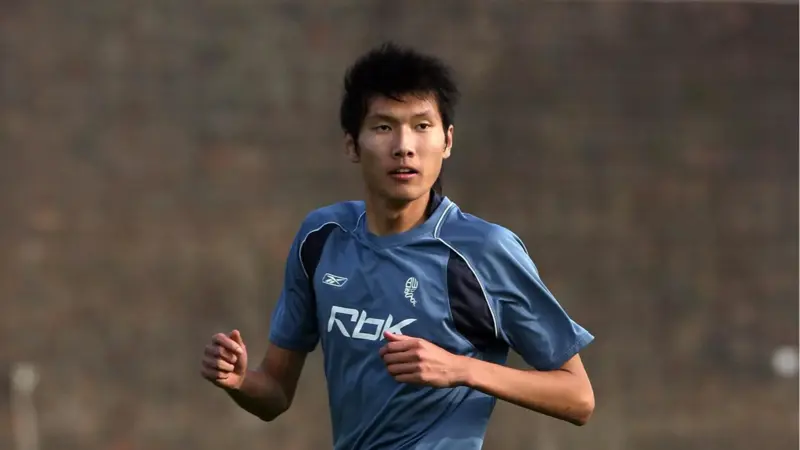 間違いなく、この中国人は史上最も背の高いサッカー選手一人だ。, 2019年に引退した同選手の身長は205センチ。, ヘディングが得意なスターストライカーだった。, その長身から、チームメイトから良くハイボールを受けていた。, もちろん、ヘディングで競り勝つのは難しい。, テクニックは劣ったが、長身のおかげで活躍。, この身長では機敏に動くことはできなかった。, 2006年にボルトンのセレクションを受けたが、残念ながら落選。, 2008年武漢でデビュー。, キャリア通算86試合に出場し、12ゴールをマークした。, 残念ながら、国際的な試合でインパクトを与えることはできなかった。