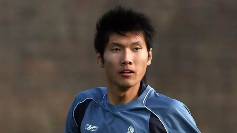 間違いなく、この中国人は史上最も背の高いサッカー選手一人だ。, 2019年に引退した同選手の身長は205センチ。, ヘディングが得意なスターストライカーだった。, その長身から、チームメイトから良くハイボールを受けていた。, もちろん、ヘディングで競り勝つのは難しい。, テクニックは劣ったが、長身のおかげで活躍。, この身長では機敏に動くことはできなかった。, 2006年にボルトンのセレクションを受けたが、残念ながら落選。, 2008年武漢でデビュー。, キャリア通算86試合に出場し、12ゴールをマークした。, 残念ながら、国際的な試合でインパクトを与えることはできなかった。