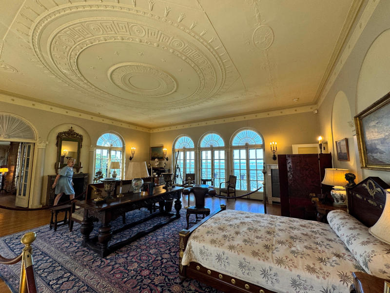 This was William II's bedroom. The room is bright, with beautiful views of the water — he probably had a great view of his 264-foot yacht, the Alva. Inside the grounds are hiking trails, gardens, and a gift shop., Before I toured the home, I visited the museum grounds., But the landscaping was still immaculate., Then it was time to head over to Eagle's Nest., One side of the mansion is a natural history museum., The first room I saw was the dining room., The ceiling is constructed from Florida cedar, or Southern Red cedar., This is her changing room and bathroom., The house was set on a hill, so the yard was multi-level., First, I walked to the right., There was a large reflecting pool., But the main attraction was, once again, the view., To my surprise, it was a filled-in saltwater pool., They'd even left the ladder in., There were also changing rooms.