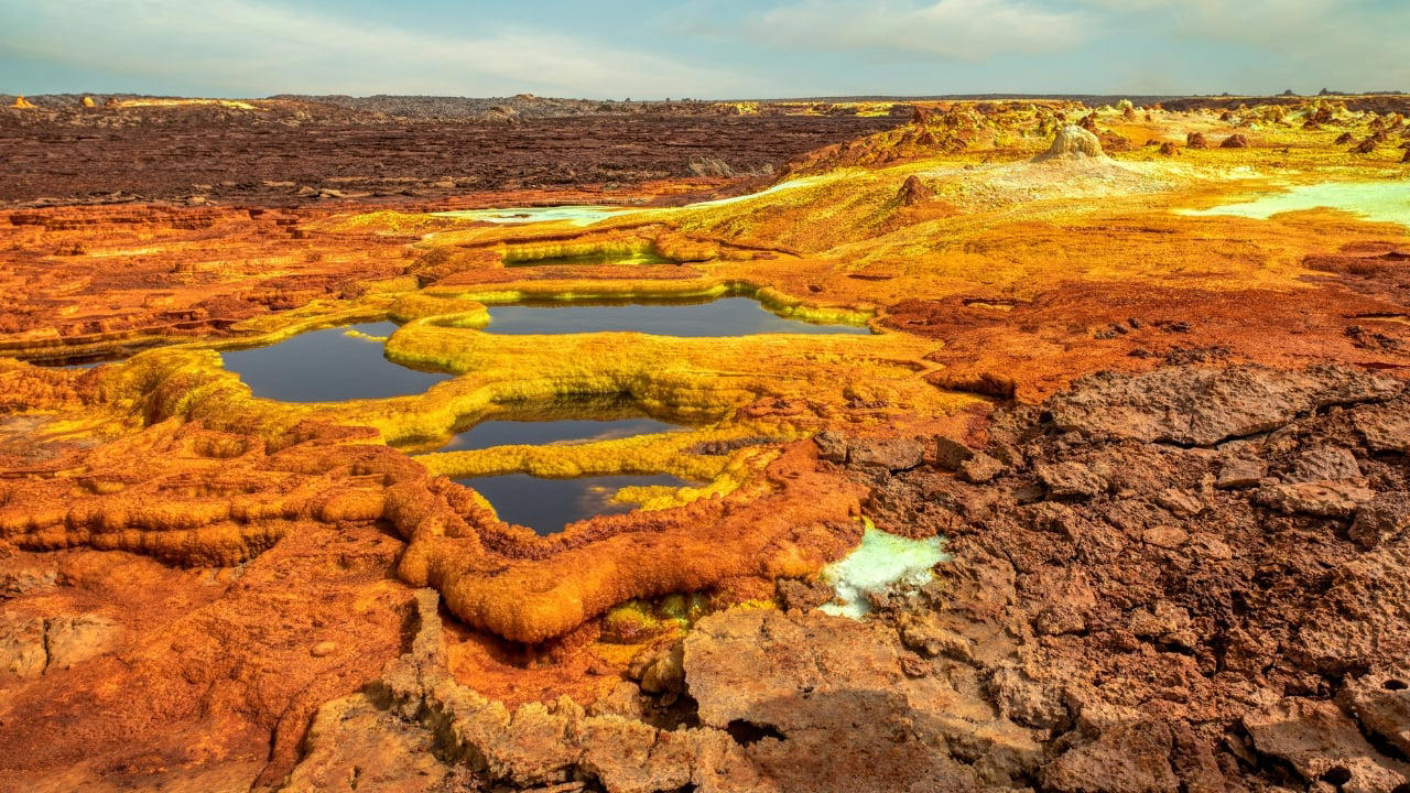 5. Dallol, Ethiopia Dallol, located in the Danakil Depression, holds the record for the highest average annual temperature ever recorded. With its sulphuric pools, neon mineral crusts, and geysers of toxic steam, it resembles a science fiction set more than a human habitat. Though now uninhabited, nomads and salt miners still pass through, navigating an area where rainfall is virtually nonexistent and the air can scald. (Image: Canva) 2. La Rinconada, Peru Perched at nearly 17,000 feet above sea level, La Rinconada is the highest permanent settlement on Earth. The thin atmosphere makes every breath laborious, while year-round sub-zero temperatures render daily tasks arduous. Its unregulated gold mines attract thousands despite the absence of basic infrastructure. Mercury contamination, lack of sanitation, and oxygen deprivation are part of daily life in this mountain outpost often described as purgatory on Earth. (Image: Wikipedia), 3. Yakutsk, Russia Situated deep in Siberia, Yakutsk is the coldest major city in the world. Winter temperatures routinely plunge below -40°C, freezing skin in mere moments. Homes are built on stilts to avoid melting the permafrost, and vehicles must be kept running to prevent their engines from freezing solid. Yet, over 340,000 people call it home, adapting with ingenuity and endurance to an environment that offers neither forgiveness nor reprieve. (Image: Canva), 4. Norilsk, Russia Locked behind the Arctic Circle, Norilsk is both remote and toxic. Established as a mining town, it suffers from some of the world’s worst industrial pollution. Residents breathe in sulfur-laced air while black snow falls during winter. The city endures a 45-day polar night, and the landscape within a 30-mile radius is barren due to acid rain. It remains a closed city, inaccessible without official permission. (Image: Canva), 5. Dallol, Ethiopia Dallol, located in the Danakil Depression, holds the record for the highest average annual temperature ever recorded. With its sulphuric pools, neon mineral crusts, and geysers of toxic steam, it resembles a science fiction set more than a human habitat. Though now uninhabited, nomads and salt miners still pass through, navigating an area where rainfall is virtually nonexistent and the air can scald. (Image: Canva), 6. Ittoqqortoormiit, Greenland Remote and ice-bound for much of the year, this settlement is a study in isolation. Home to roughly 350 people, it can only be reached by helicopter or boat during brief windows of accessibility. Winter darkness lasts for months, temperatures plummet, and polar bears pose a very real threat. Emergency evacuations are perilous, and the nearest neighbouring town is 300 miles away. (Image: Canva), 8. Chernobyl, Ukraine Within the Chernobyl Exclusion Zone, a small number of elderly inhabitants defy radiation and time. After the 1986 meltdown, most fled. Some, however, returned to reclaim their homes, despite radiation levels still far exceeding safety norms. These residents live without running water or medical care, growing food in contaminated soil. Their lives carry the quiet defiance of those who have outlived disaster. (Image: Canva), 9. Dharavi, Mumbai, India Spanning less than a square mile, Dharavi houses close to a million people, making it one of the most densely packed urban areas on Earth. Narrow alleys, unregulated electricity, and poor sanitation foster conditions ripe for fire, flood, and disease. Despite its challenges, Dharavi is also an economic engine—home to thousands of micro-industries producing textiles, pottery, and recycled goods worth over a billion dollars annually. (Image: Canva), 10. Villa Las Estrellas, Antarctica Located on King George Island, this Chilean settlement resembles a scientific outpost more than a town. Long-term residents must undergo appendectomies before arriving, as medical facilities are rudimentary and evacuations impossible in winter. Here, families endure endless nights, hurricane-force winds, and frigid temperatures, living in prefabricated homes amid one of Earth’s most hostile environments. (Image: Wikipedia), 11. Barrow (Utqiaġvik), Alaska, USA The northernmost city in the United States lives in the shadow of disappearing coastlines and encroaching darkness. Barrow experiences more than two months without sunlight each winter. Supply chains are fragile, with most goods arriving by air. Climate change has turned the surrounding permafrost into sinking land, while sea ice retreats leave it more exposed to erosion. Yet life here persists—rugged, quiet, and enduring. (Image: Canva)
