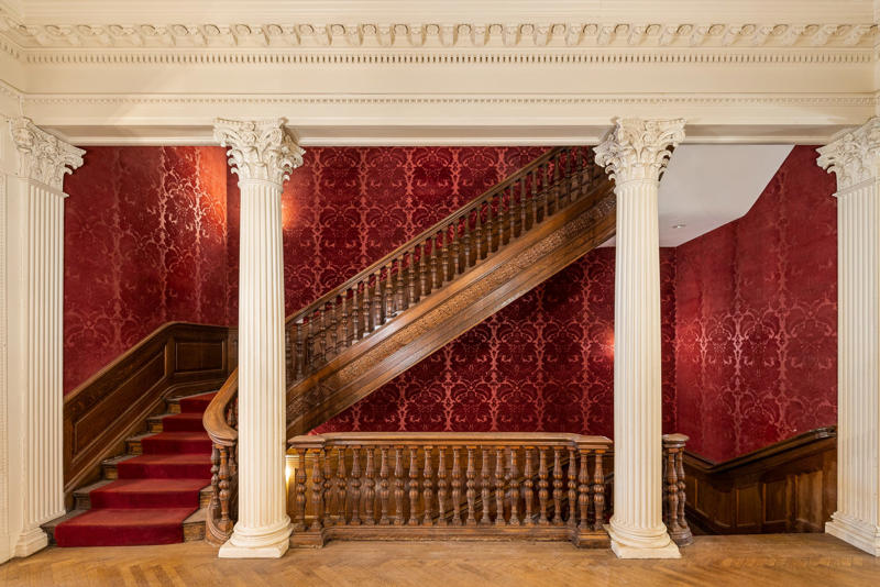 Neo-Georgian architectural touches include columns and decorative molding known as cornices. The five-story townhouse is located across from the Museum of Modern Art., The entry gallery on the first floor features wood paneling throughout., Neo-Georgian architectural touches include columns and decorative molding known as cornices., Two staircases lead to the upper floors., Rooms on the upper floors feature floor-to-ceiling windows and Juliet balconies., The dining room is shaped like an octagon.