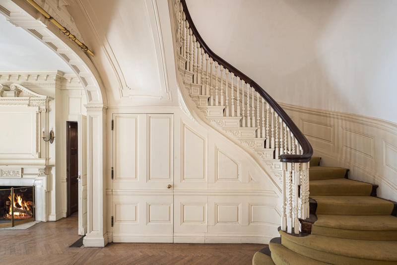 Two staircases lead to the upper floors. The five-story townhouse is located across from the Museum of Modern Art., The entry gallery on the first floor features wood paneling throughout., Neo-Georgian architectural touches include columns and decorative molding known as cornices., Two staircases lead to the upper floors., Rooms on the upper floors feature floor-to-ceiling windows and Juliet balconies., The dining room is shaped like an octagon.