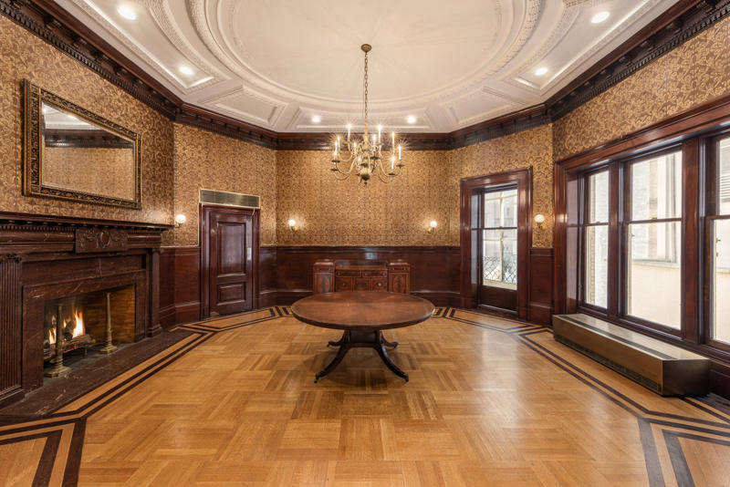 The dining room is shaped like an octagon. The five-story townhouse is located across from the Museum of Modern Art., The entry gallery on the first floor features wood paneling throughout., Neo-Georgian architectural touches include columns and decorative molding known as cornices., Two staircases lead to the upper floors., Rooms on the upper floors feature floor-to-ceiling windows and Juliet balconies., The dining room is shaped like an octagon.