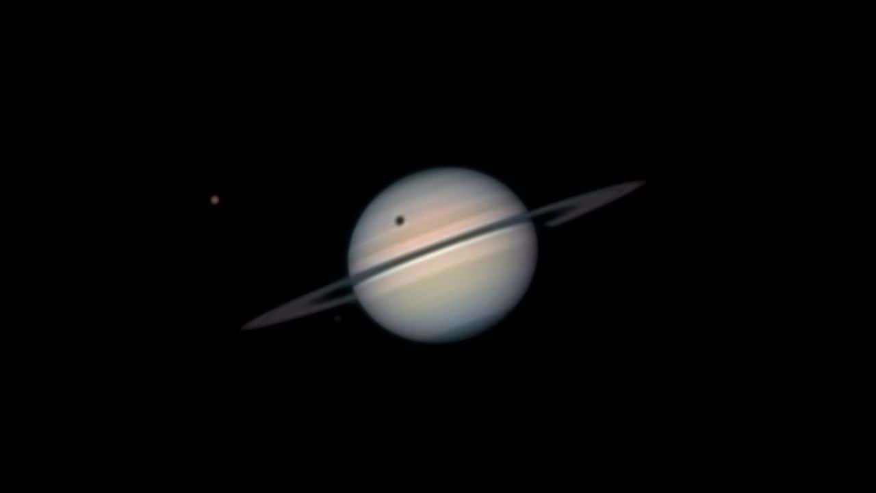 Titan Shadow Transit: Saturn’s moon Titan casts a shadow across the planet’s surface during its transit season, offering rare views as Saturn’s rings tilt edge-on every 15 years. (Image: NASA)