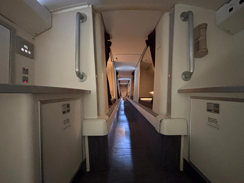 It was slightly eerie looking down the dim and lengthy corridor. The door opens to reveal a steep and narrow staircase., It was slightly eerie looking down the dim and lengthy corridor., However, the beds themselves didn't look too uncomfortable., Each bed had pockets for storage, a coat hook, and a mirror.