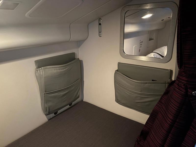 Each bed had pockets for storage, a coat hook, and a mirror. The door opens to reveal a steep and narrow staircase., It was slightly eerie looking down the dim and lengthy corridor., However, the beds themselves didn't look too uncomfortable., Each bed had pockets for storage, a coat hook, and a mirror.
