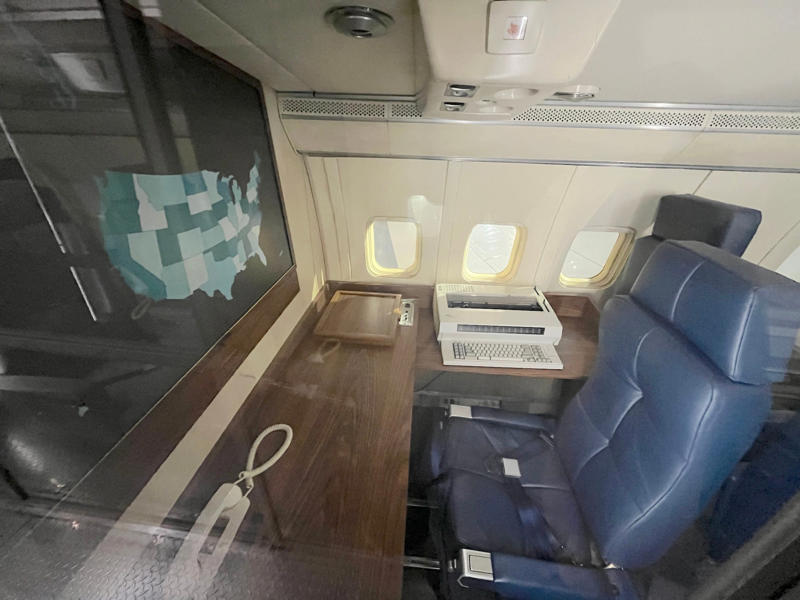 An office area across the aisle featured an electric typewriter, scanner, and more phones. Two phones were located behind the flight deck., An equipment storage space featured a first aid kit and firearms., Next, I walked by the plane's communication facility., Meals were prepared in the galley., The presidential stateroom was located down a long hallway., The president's spacious quarters featured a desk, couch, television, and private bathroom., The stateroom came with two phones, each with different purposes., Behind the presidential stateroom, a conference room provided more meeting space.