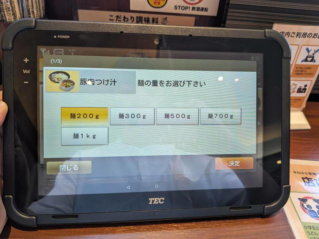 猫も杓子も体験…やたら「体験」を推す外食企業, 新業態1号店は堅実に郊外ロードサイド, オープンから半月経過も行列ができる人気ぶり, 注文はタブレット、上げ膳・下げ膳まですべてお客がやる, 1000円前後で食べ放題付きはお得, 「豚肉つけ汁うどん」1089円はこんな感じ, 従来のうどんチェーンは注文に高度な意思決定が求められる？, 意思決定が負担、でも失敗したくない…現代人のニーズに合ううどん店