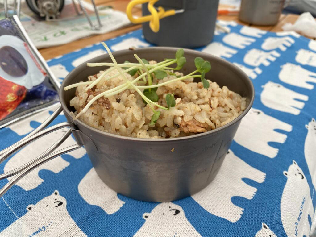 キャンプでご飯を炊く前に！まずは基本の道具を知ろう, 炊飯に必要な「基本セット」, 道具のメリット・デメリット, キャンプで失敗せずに美味しくご飯を炊くコツ, 1.米と水の「計量」は正確に行う, 2.「吸水」を最低30分（冬場は1時間）は行う, 3.火加減は「沸騰するまで中火 → 沸騰したら弱火」, 4.炊飯中は「絶対に蓋を開けない」, 5.火から下ろしたら「必ず10分以上蒸らす」, 【道具別】炊き方ガイド｜メスティン・飯ごう・鍋・ライスクッカー・ダッチオーブン, 鍋（クッカー）は重しを使うのがポイント, 飯ごうは蓋で軽量もできるのがポイント, メスティンは火加減がポイント, ライスクッカーは機能をフル活用するのがポイント, ダッチオーブンは蓋の上に炭を置くのがポイント, もっと美味しく！キャンプで食べたい絶品ご飯レシピ, 缶詰ひとつで味が決まる！超簡単「炊き込みご飯」, 「お焦げ」も「残りご飯」もごちそうに！翌朝活用レシピ, 美味しいご飯が、キャンプをもっと楽しくする