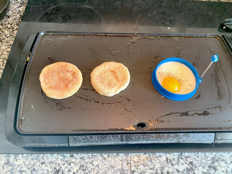 Marchand's bacon and egg muffin requires just a few main ingredients., To begin, I first cooked my bacon., As the bacon started cooking, I prepped my English muffins., Then it was time to start building the sandwich., Once the cheddar slices had softened, it was time for some saucin'., Then I added the bacon slices., I plopped my egg right on top of the bacon.