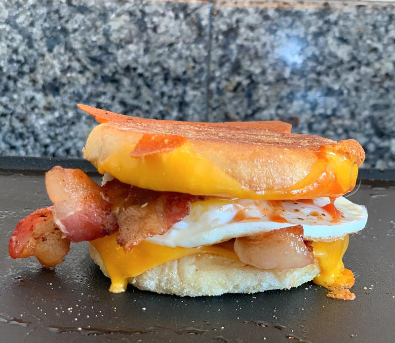Marchand's bacon and egg muffin requires just a few main ingredients., To begin, I first cooked my bacon., As the bacon started cooking, I prepped my English muffins., Then it was time to start building the sandwich., Once the cheddar slices had softened, it was time for some saucin'., Then I added the bacon slices., I plopped my egg right on top of the bacon.