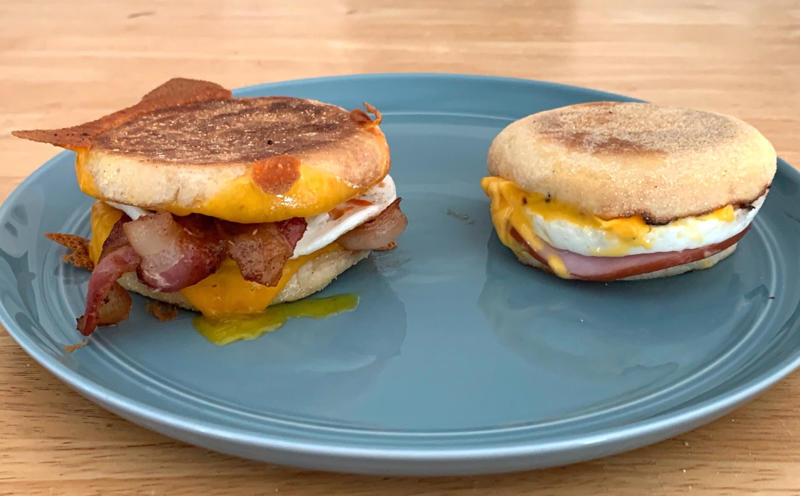Marchand's bacon and egg muffin requires just a few main ingredients., To begin, I first cooked my bacon., As the bacon started cooking, I prepped my English muffins., Then it was time to start building the sandwich., Once the cheddar slices had softened, it was time for some saucin'., Then I added the bacon slices., I plopped my egg right on top of the bacon.