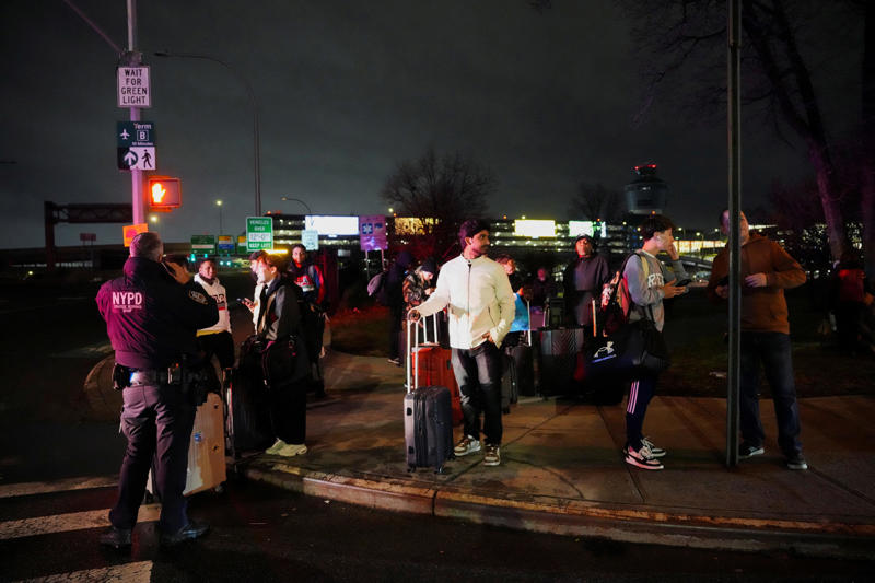 Passengers wait outside a police cordon, on the day an Air Canada Express jet collided with a ground vehicle at New York's LaGuardia Airport, March 23, 2026.