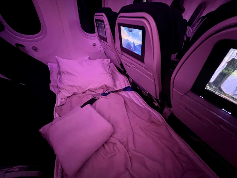 ANZ's Skycouch view from the aisle. The Skynest will be located in the middle of the plane., It features curtains, power, and a seatbelt., Flyers get soft linens and an amenity kit., I'd prefer the bottom or middle bunks., Flyers will eat before or after their block., You must be 15 or older., I'd book the Skynest to fight jet lag., The Skynest is ANZ's second economy bed.