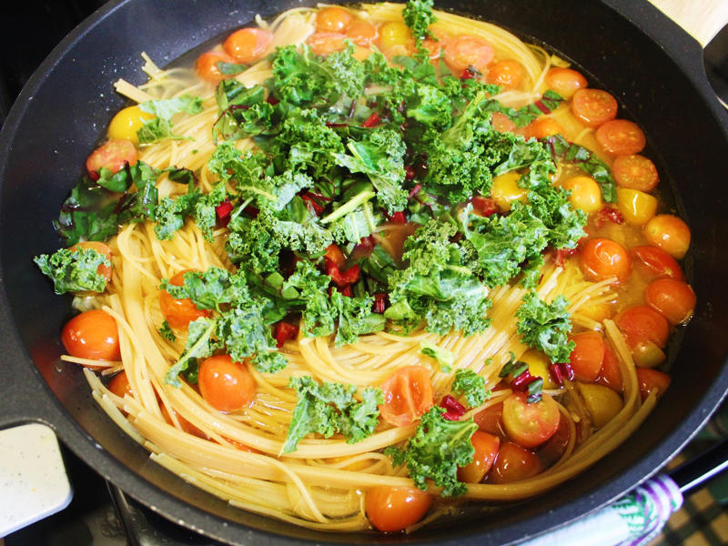 When the pasta was fully brought to a boil, I lowered the heat and added the greens. I started by gathering the ingredients for the one-pot pasta., I chopped the tomatoes in half and added them to my skillet., I then added about a box of spaghetti to the pan., While the pasta was cooking, I chopped the Swiss chard.
