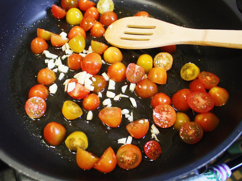 I added the tomatoes to my skillet with chopped garlic and olive oil. I started by gathering the ingredients for the one-pot pasta., I chopped the tomatoes in half and added them to my skillet., I then added about a box of spaghetti to the pan., While the pasta was cooking, I chopped the Swiss chard.