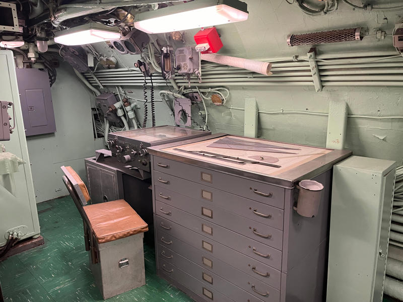 In the navigation compartment, crew members plotted courses and tracked Growler's position. In the navigation compartment, crew members plotted courses and tracked Growler's position., The missile checkout and guidance center was once a top-secret area., Officers had access to their own shower., Officers used the wardroom to eat, socialize, and hold meetings., Yeomen handled clerical and administrative work aboard the USS Growler's tiny office., Here, the commanding officer would give orders to the crew., The sonar room also aided Growler's navigation., Crew members communicated with other ships in the radio room., Meals were prepared in the galley., In the scullery, Growler crew members washed dishes and compacted trash., The crew's mess was the only common space on the USS Growler., Growler's largest sleeping area contained 46 bunks., The crew's washroom featured two showers., Growler's three diesel engines were located in the engine room.