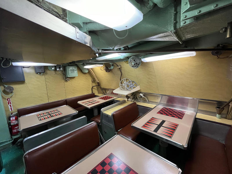 The crew's mess was the only common space on the USS Growler. In the navigation compartment, crew members plotted courses and tracked Growler's position., The missile checkout and guidance center was once a top-secret area., Officers had access to their own shower., Officers used the wardroom to eat, socialize, and hold meetings., Yeomen handled clerical and administrative work aboard the USS Growler's tiny office., Here, the commanding officer would give orders to the crew., The sonar room also aided Growler's navigation., Crew members communicated with other ships in the radio room., Meals were prepared in the galley., In the scullery, Growler crew members washed dishes and compacted trash., The crew's mess was the only common space on the USS Growler., Growler's largest sleeping area contained 46 bunks., The crew's washroom featured two showers., Growler's three diesel engines were located in the engine room.