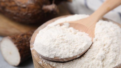 Wooden bowl and spoon with cassava flour on table&comma; closeup